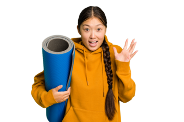 Young asian sport woman holding a mat isolated receiving a pleasant surprise, excited and raising hands.