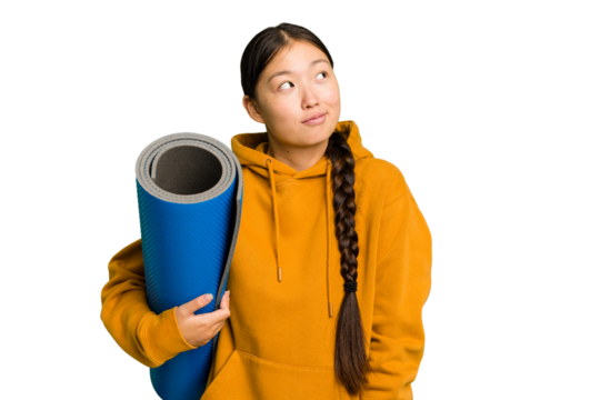 Young asian sport woman holding a mat isolated dreaming of achieving goals and purposes