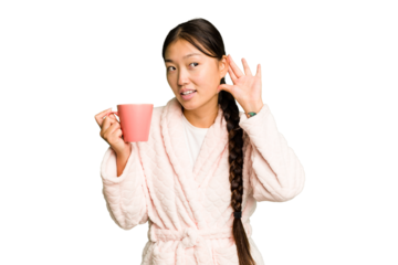 Young asian woman wearing a pajama holding a cup isolated trying to listening a gossip.