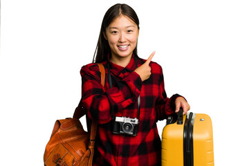 Traveler asian woman holding a suitcase isolated smiling and pointing aside, showing something at...