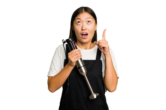 Young asian cook woman holding a blender isolated pointing upside with opened mouth.