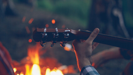 Close-up shot of male tourist's hand playing the guitar during romantic evening at campsite with...