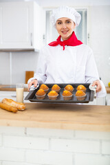Happy female pastry chef with tray of cupcakes