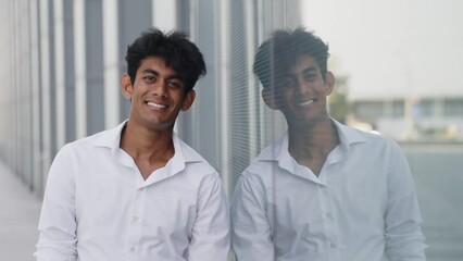 Happy stylish businessman standing near office building with his reflection