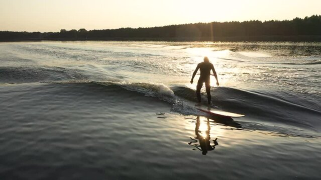 surfer on longboard surfing wave behind boat with cross step in sunset