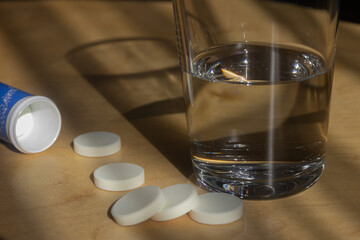 Tablets and a glass of water on a wooden table, vitamin or mineral supplements, medicines spilling from the box, selective focus
