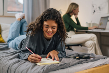 smiling teenager female does home work in dorm room