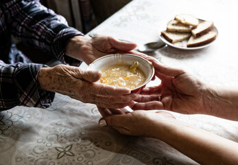 Volunteer gives food to senior at old people house; fragment photo of hands doctor giving soup to...