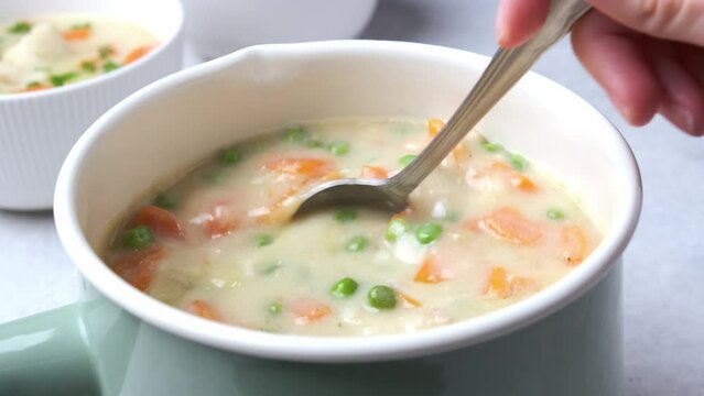 Fish cod chowder soup with green peas, potatoes and carrots in blue saucepan.