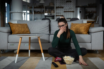 Young scared woman sitting alone at home on the floor watching scary horror movie on the television. Disgusted animal lover female saw animal cruelty tv show feeling sad, disturbed, sorry for animals.