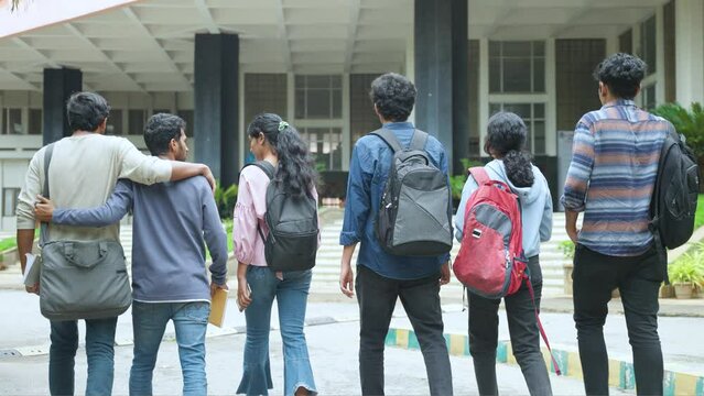 Back view tracking shot of students with backpack going to classroom at college campus - concept of back to school, friendship and education.