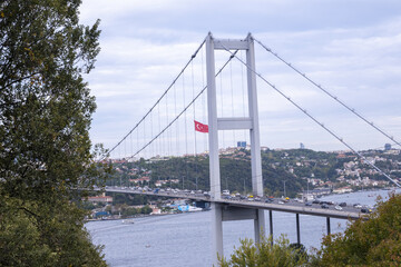 Fototapeta premium Close-up Istanbul Bosphorus and landscape view from Nakkastepe National Garden, Trees and cloudy weather, Istanbul tourism banner, 15th of July Martyrs Bridge, transportation idea