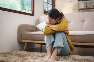 Young Asian woman suffering from work stress sits alone on the sofa at home discouraged. Desperate...