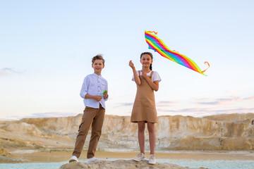 A boy and a girl are standing with a kite high stone near the lake.