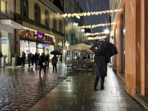 Night city street man with umbrella walk on medieval street house festive garland and first snow with rain in Tallinn old town travel Eston
