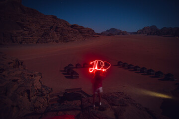 Traveler dreamer adventurer in wadi rum desert at night light painting word JO as Jordan with...