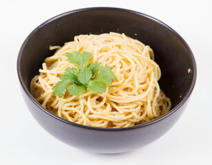 Yellow pepper pesto spaghetti decorated with coriander in a black bowl on a white background