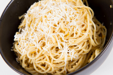 Yellow pepper pesto spaghetti covered with grated mozzarella cheese in a black bowl on a white...