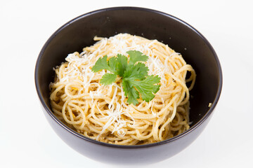Yellow pepper pesto spaghetti covered with grated mozzarella cheese decorated with coriander in a black bowl on a white background