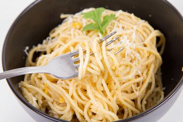 Yellow pepper pesto spaghetti covered with grated mozzarella cheese decorated with coriander being rolled around a fork