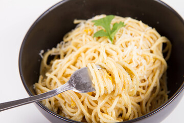Yellow pepper pesto spaghetti covered with grated mozzarella cheese decorated with coriander being rolled around a fork