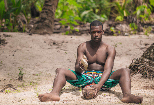 Black man hitting a coconut with a stone