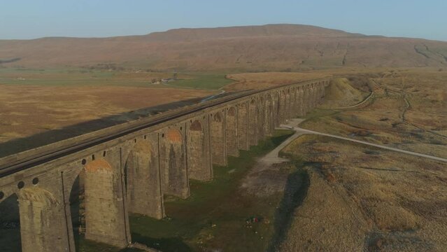 Aerial Drone Shot Along Ribblehead Viaduct Train Bridge at Stunning Sunrise with long shadows in Summer in Yorkshire Dales England UK with 3 Peaks Whernside Mountain in Background
