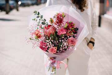 Very nice young woman holding beautiful bouquet of fresh eucalypts, roses, baby breath, eustoma,...