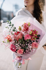 Very nice young woman holding beautiful bouquet of fresh eucalypts, roses, baby breath, eustoma, Protea, tender flowers in pink colors, cropped photo, bouquet close up - 542687664
