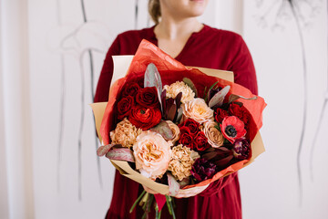 Very nice young woman in a red dress holding beautiful bouquet of fresh anemone, carnations, roses, leukadendron flowers in red and pastel brown colors, cropped photo, bouquet close up - 542687677