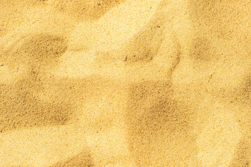 Fototapeta na wymiar Close-up of a sandy beach. Background with sand unevenly swept away by wind and waves into small dunes. Background for a cover or design on the theme of travel.