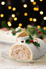 White chocolate yule log cake with christmas lights and ornaments on wooden table. Copy space