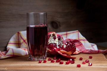 Fresh red pomegranate and glass of fresh rudy juice on a wooden background..