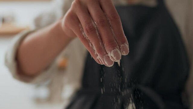 Hand throws dry flour, falling white dust of flour, hand of the cook pours white flour on the dough, Preparing dough for baking pizza pie bread
