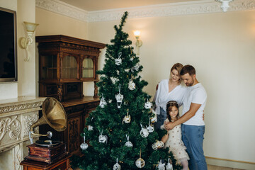 Family decorating a Christmas tree. Young man with his daughter on his shoulders helping her decorate the Christmas tree.