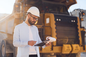 In glasses, reading documents. Man in uniform is working in the quarry at daytime