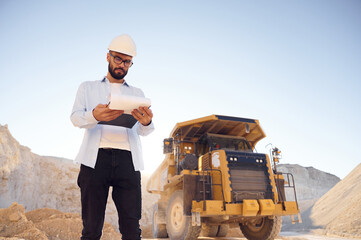 Smart person is with documents in hands. Man in uniform is working in the quarry at daytime