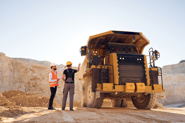 Standing near haul truck and talking about document. Two men in uniform are working together in the...