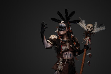 Studio shot of dark voodoo witch with painted face holding staff.