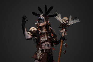Portrait of spooky voodoo necromancer dressed in dark clothes holding staff with skull.