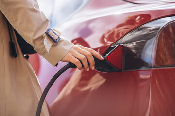 Woman holding charging pistilol and charging electric car