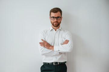 Elegant man in white shirt, black pants and in eyewear is standing against white wall