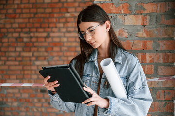 With plan in hands. Young woman is standing in the unfinished building on construction site and working on a project