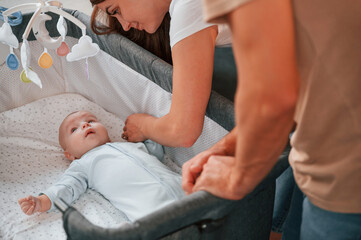 Looks down at the kids. Lovely couple taking care of newborn baby indoors at domestic room