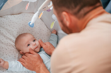 Newborn baby is in the cradle. Father is indoors. Conception of single dad