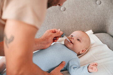 Gives medicine with a pipette. Father with his newborn baby is indoors. Conception of single dad