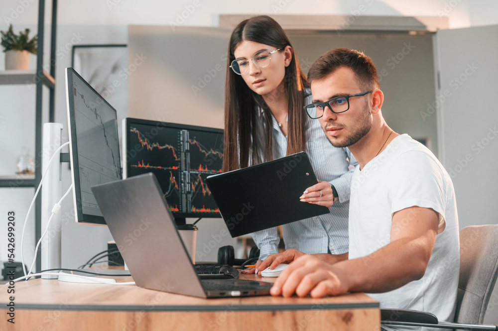 Poster analyzing information from computer screens. two stock brokers is working together in the office wit