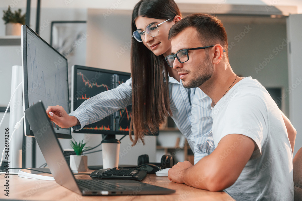 Poster analyzing information from computer screens. two stock brokers is working together in the office wit