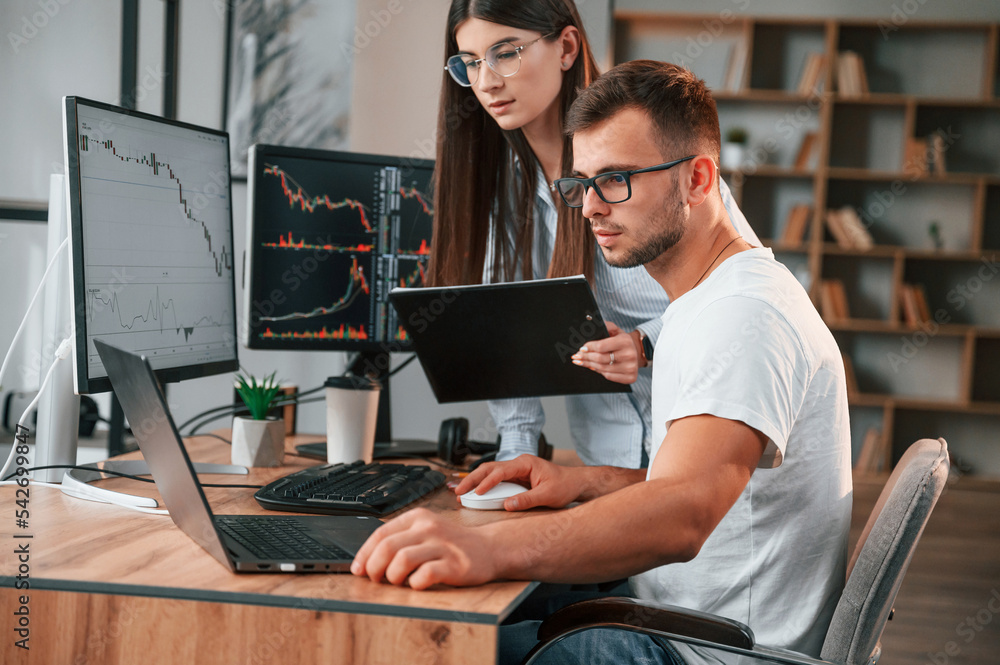 Poster analyzing information from computer screens. two stock brokers is working together in the office wit