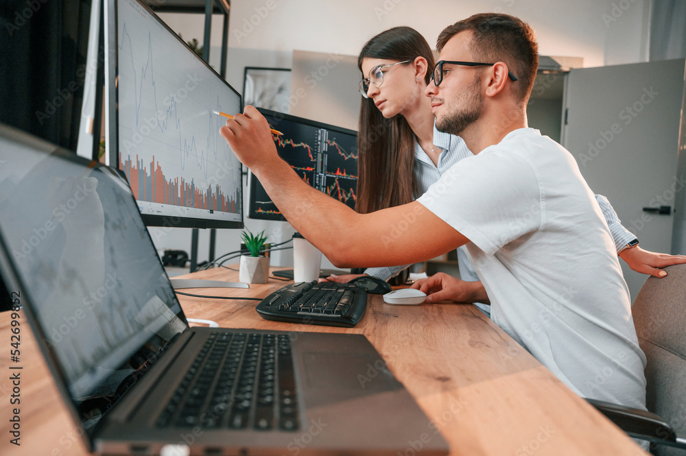 Poster analyzing information from computer screens. two stock brokers is working together in the office wit